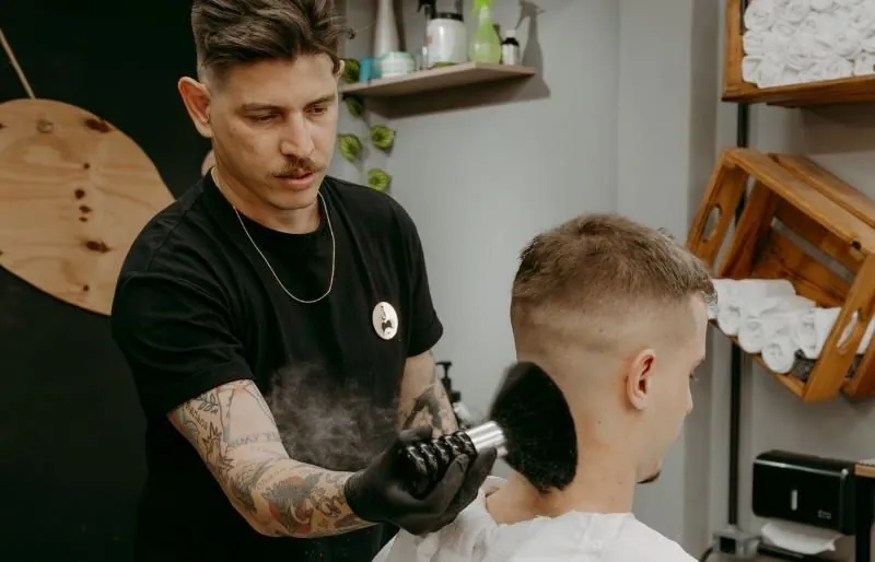 Barbeiro limpando a nuca do cliente com pincel após o corte