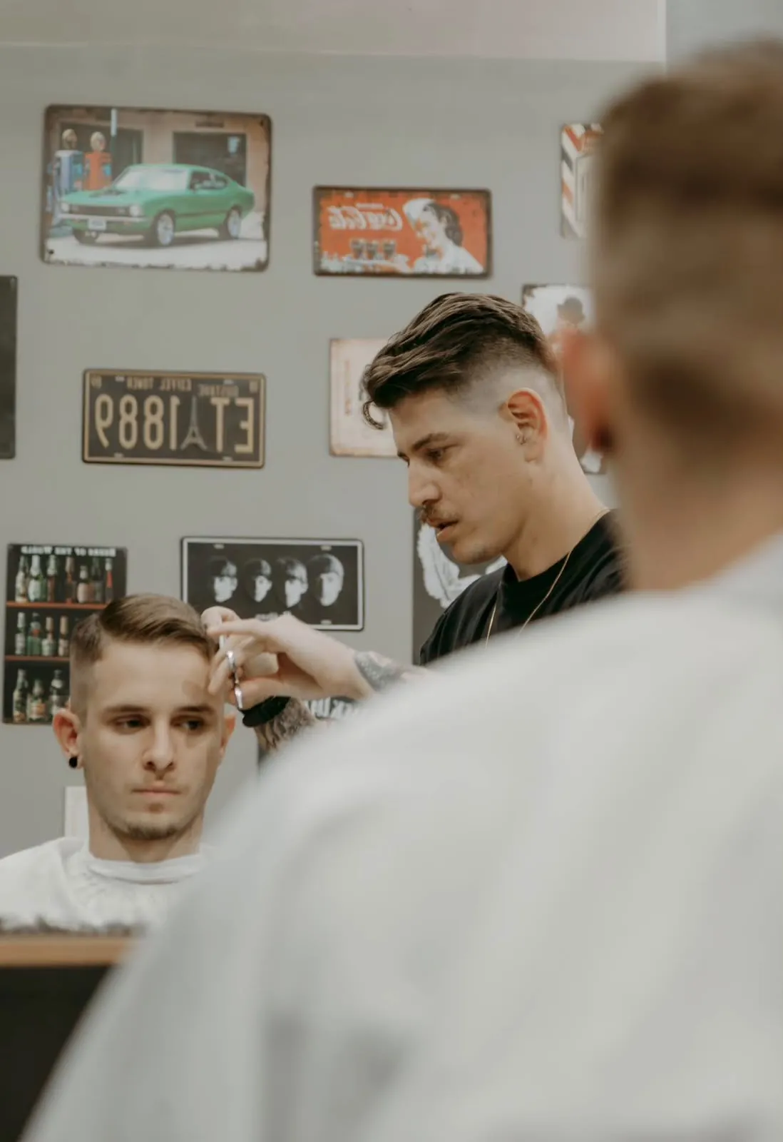 Barbeiro finalizando um corte na tesoura, com placas vintage na parede ao fundo