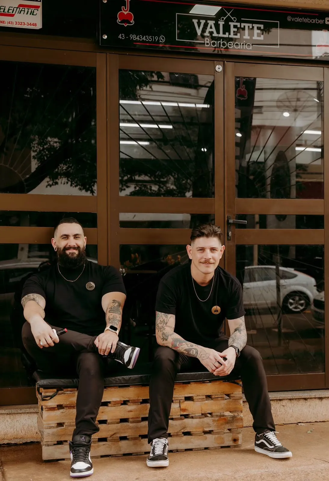 Fachada da Valete Barbearia com os dois barbeiros sentados em frente à porta