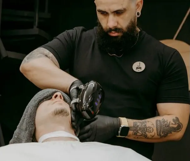 Barbeiro fazendo limpeza de pele em um cliente com aparelho facial